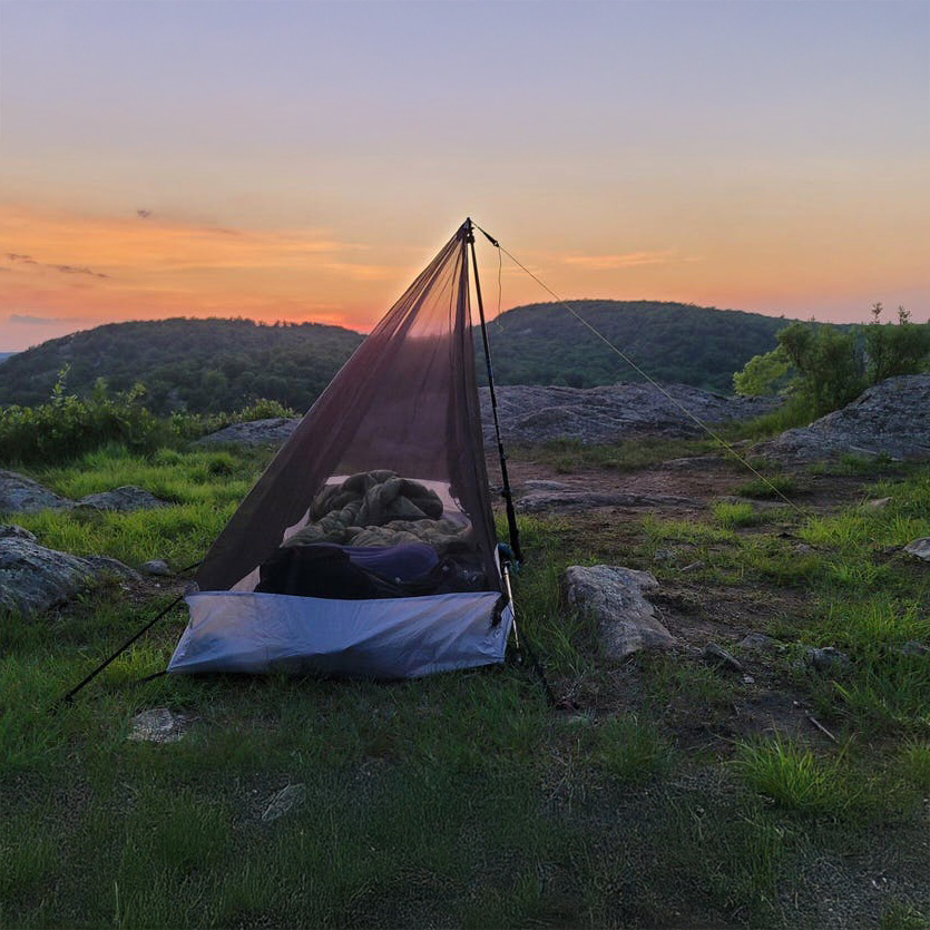Six Moon Designs Serenity NetTent ultralight solo mesh inner tent pitched on a grassy mountain ridge during a dramatic sunset.